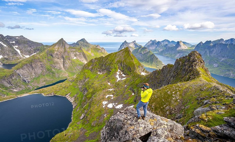 Mountaineer photographed at the summit of Munken, mountain landscape with steep rocky mountain peaks, lake Tennesvatnet fjords and sea, view from the summit of Munken to Reinefjorden, Moskenesoya, Lofoten, Nordland, Norway, Europe