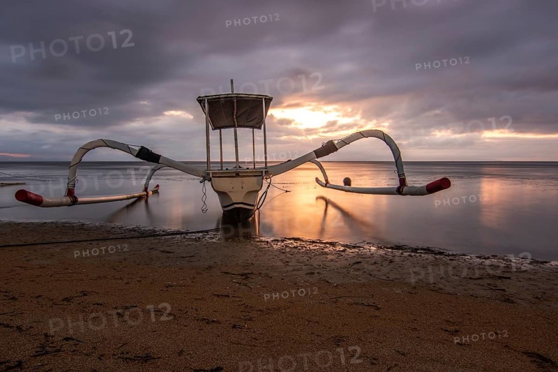 Jukung in the sea, typical landscape shot with a view of the horizon over the water, taken from a sandy beach. Traditional fishing boat at sunrise. Landscape shot of Sanur, Bali, Indonesia, Asia
