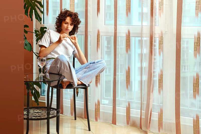 Woman examining broken fingernail sitting on chair by the window