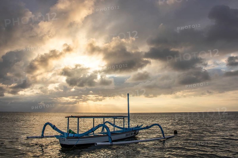 Jukung in the sea, typical landscape shot with a view of the horizon over the water, taken from a sandy beach. Traditional fishing boat at sunrise. Landscape shot of Sanur, Bali, Indonesia, Asia