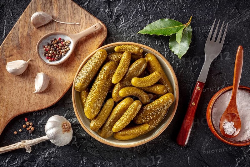 Pickled cucumbers with salt, pepper, garlic, and bay leaf. Fermented food. Homemade canned gherkins. Overhead flat lay shot on a black slate background, Food photography