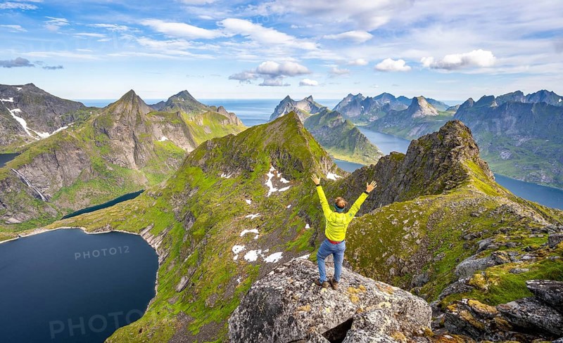 Mountaineer stretching his arms in the air, at the summit of Munken, mountain landscape with steep rocky peaks, lake Tennesvatnet fjords and sea, view from the summit of Munken to Reinefjorden, Moskenesoya, Lofoten, Nordland, Norway, Europe