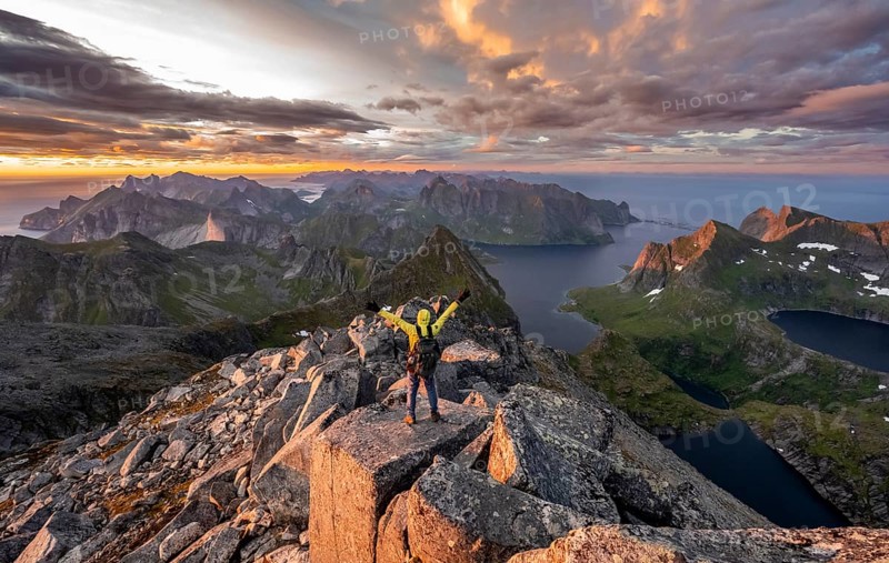 View over mountain top and sea, dramatic sunset, mountaineers at Hermannsdalstinden peak, with lakes Litlforsvatnet and Tennesvatnet and fjord Forsfjorden, Moskenesöy, Lofoten, Nordland, Norway, Europe
