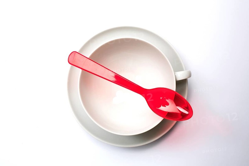 Crockery and cutlery, empty teacup with saucer, seen from above, a red plastic spoon lies on it