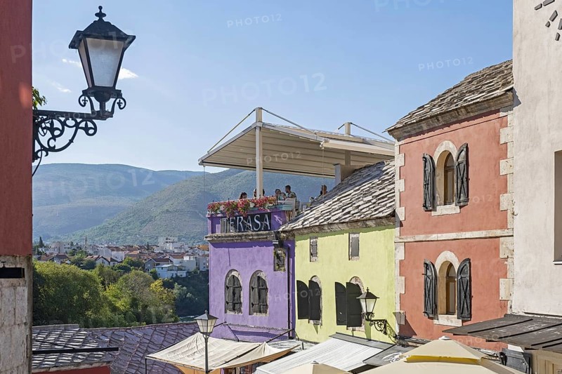 Tourists on terrace of restaurant and pastel coloured houses in the Old Town of Mostar, Herzegovina-Neretva Canton, Bosnia and Herzegovina, Europe
