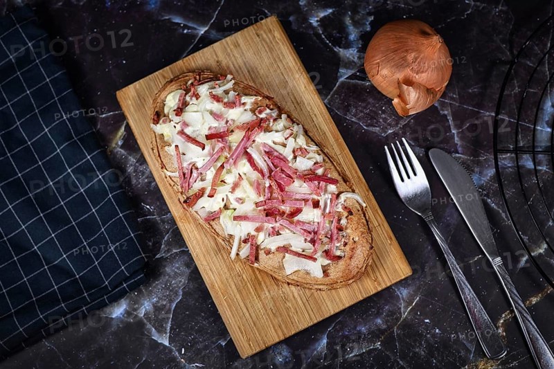 Oval shaped taditional food 'Tarte Flambee' or 'Flammkuchen' from German-French Alsace border region. The name means 'pie baked in the flames', similar to a thin pizza with bacon and soured cream