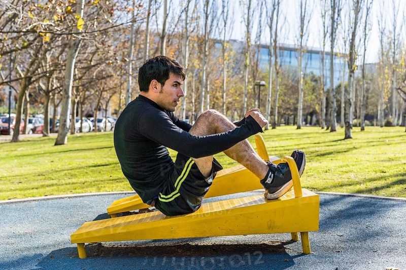 Confident young man doing abdominal exercises on a public equipment in outdoor fitness