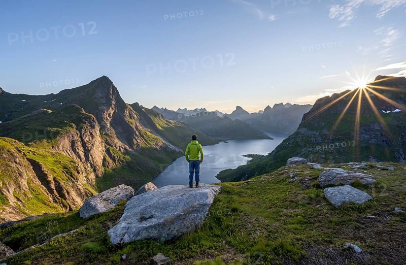 Mountaineer looking over mountain landscape with pointed mountain peaks and fjord Forsfjorden with village Vindstad, sun star at sunrise, Moskenesoya, Lofoten, Nordland, Norway, Europe