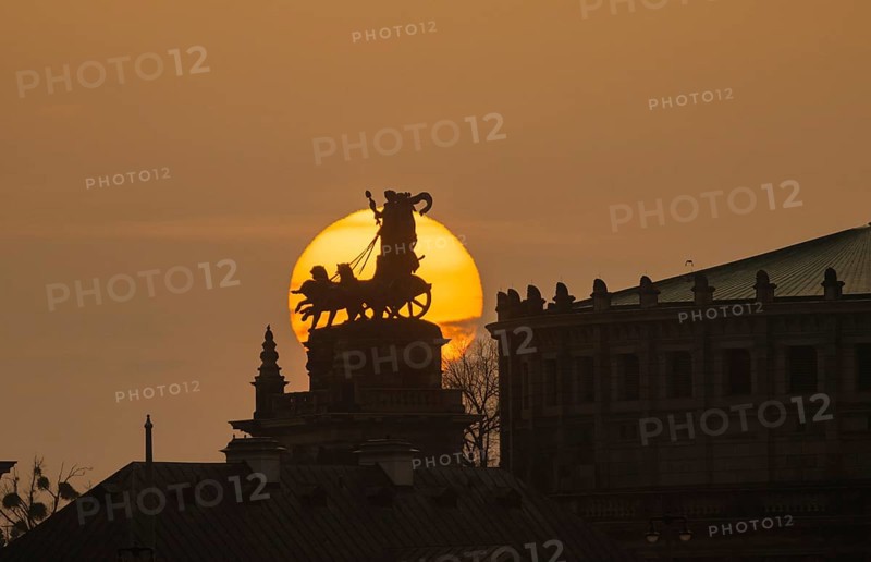 Sunset in Dresden. The sun's disc, particularly orange due to the Sahara dust, sets behind the quadriga on the portal of the Semper Opera House