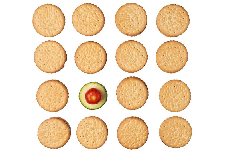 Double biscuits in rows with a courgette slice (Cucurbita pepo) and a tomato (Solanum lycopersicum), on white