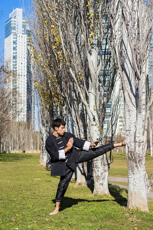 An athletic martial arts fighter practicing kicks in a public park.