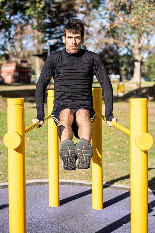 Frotn view of a young man doing abdominal exercises on a public equipment in outdoor fitness