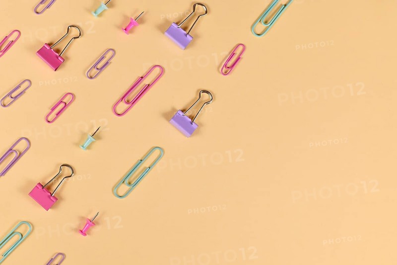 Stationery items like paper clips and drawing pins arranged on side of yellow background with empty copy space