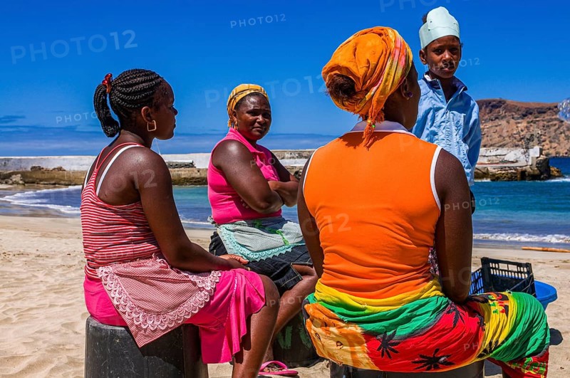 Dark skinned women, sitting at sandbeach and talking to each other. Tarrafal. Santiago. Cabo Verde. Africa