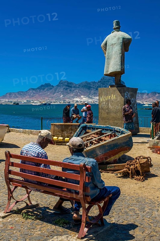 People sitting on bench in front of sculpture. San Vincente. Mindelo. Cabo Verde. Africa