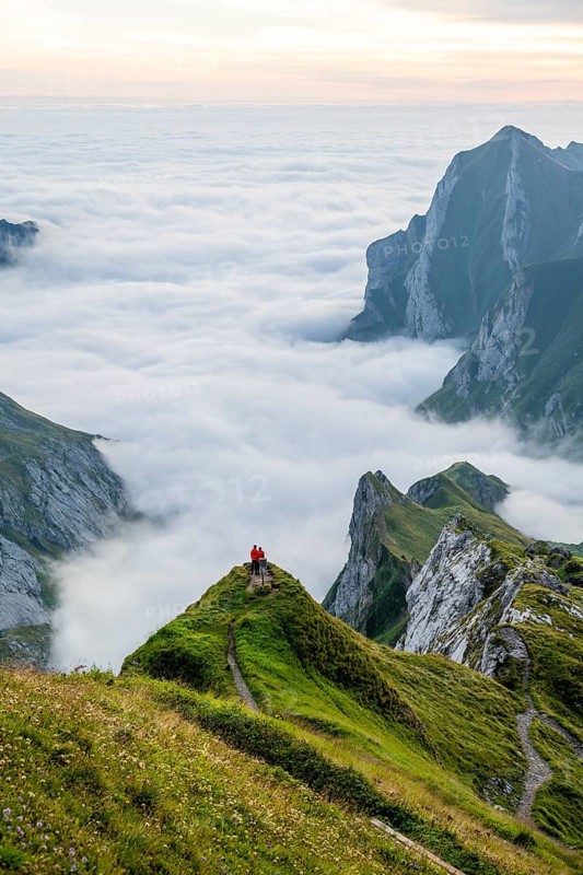 Two hikers enjoying the view over the Säntis mountains into the valley of Meglisalp at sunrise, high fog in the valley, Säntis, Appenzell Ausserrhoden, Appenzell Alps, Switzerland, Europe