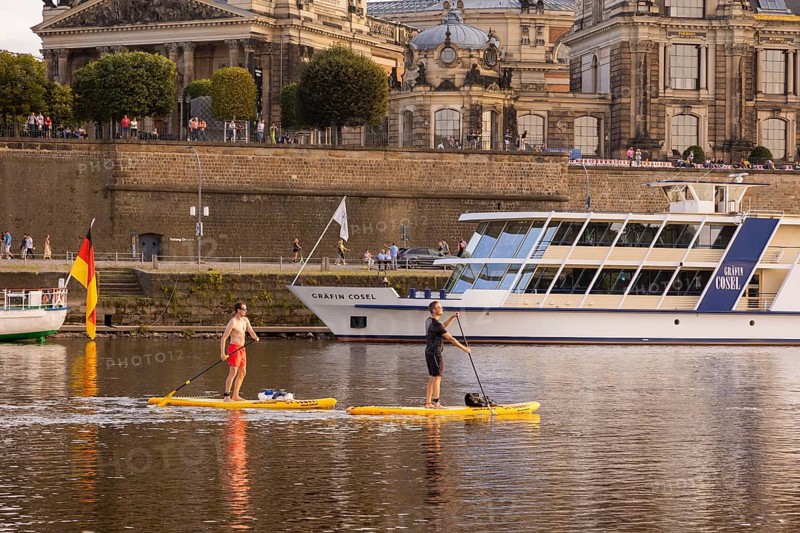 Stand-up paddlers on the Elber in front of the terrace bank with steamboats and the silhouette of the old town