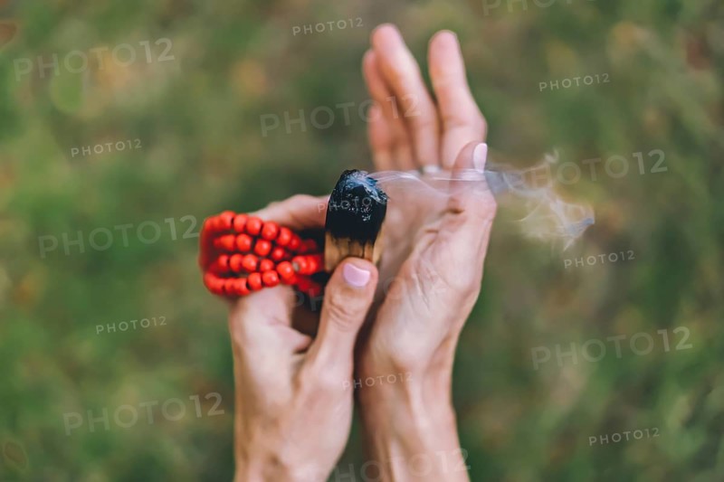 Top angle view of a palo santo or a holy sacred tree stick, burning with aroma smoke held by woman's hands over nature background