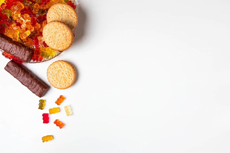 Various sweets, jelly bears, biscuits, chocolate bars, on and next to plates, white background, copying room
