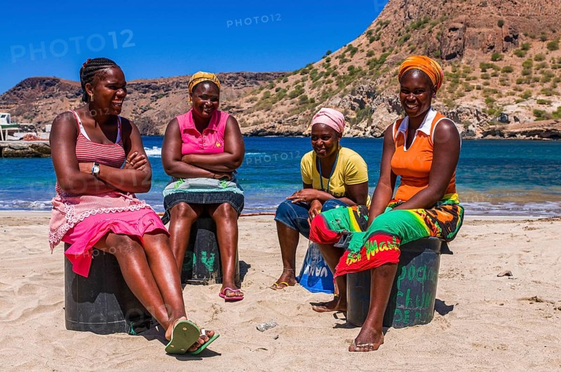 Dark skinned women, sitting at sandbeach and talking to each other. Tarrafal. Santiago. Cabo Verde. Africa