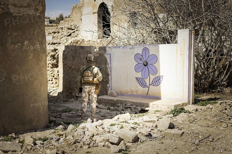 Ein Soldat steht vor einer an die Wand gemalten Blume im zerstoerten Stadtzentrum von Sinjar, 09.03.2023