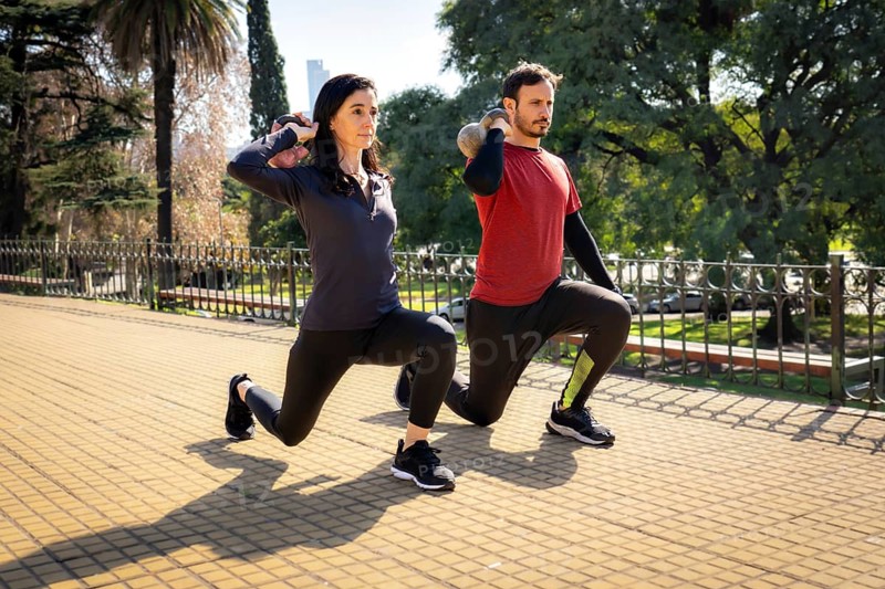 Man and woman lifting Kettlebells Together. Outdoor sports concept
