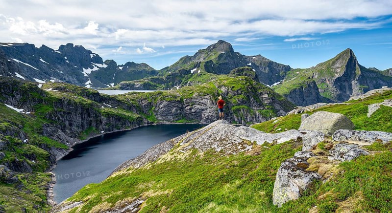 Mountaineer on a rock, mountain landscape with rocky pointed mountain peaks and lakes, with mountain Hermannsdalstinden and lakes Tennesvatnet and Krokvatnet, Moskenesoya, Lofoten, Nordland, Norway, Europe