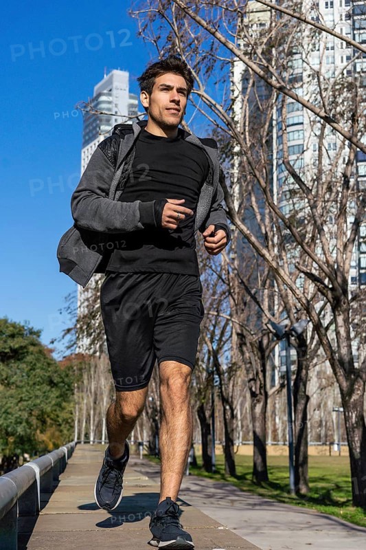Motivated handsome man jogging by green public park