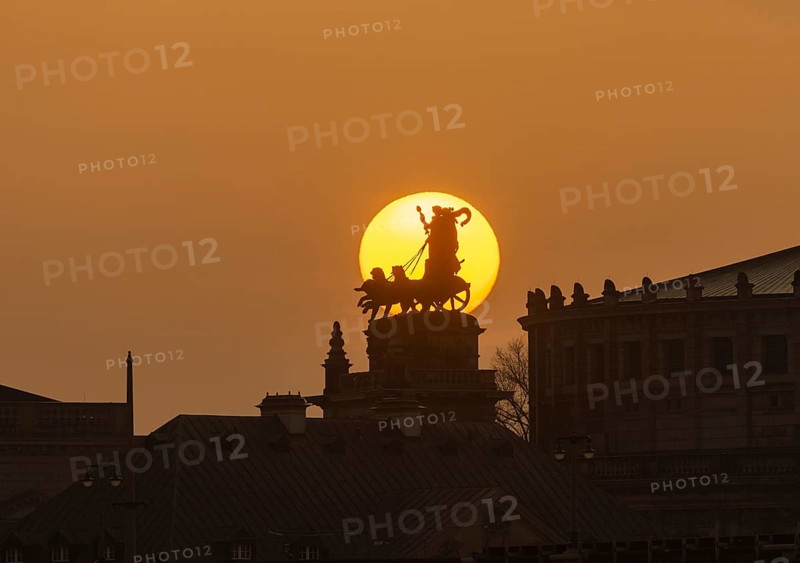 Sunset in Dresden. The sun's disc, particularly orange due to the Sahara dust, sets behind the quadriga on the portal of the Semper Opera House