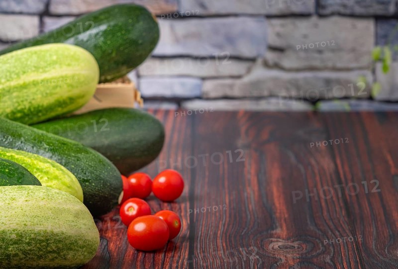 Courgettes (Cucurbita pepo), field cucumbers (Cucumis sativus), tomatoes (Solanum lycopersicum), on wood, in front of stone wall