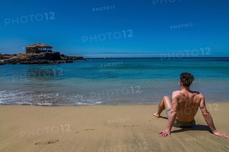Young man with bathing-trunks, sitting on sandbeach. Tarrafal. Santiago. Cabo Verde. Africa