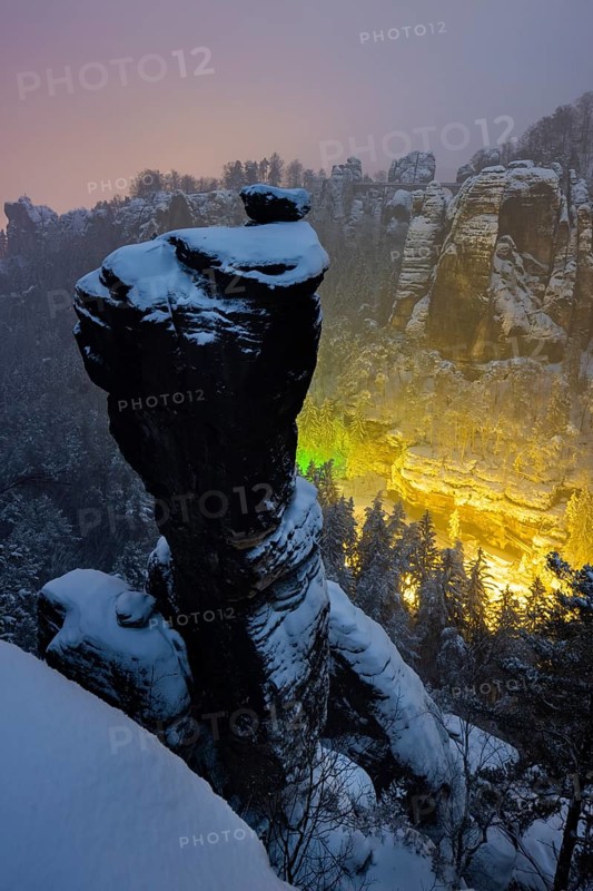 Winter in the Basteige area. The Wehlnadel rises steeply above the Wehlgrund, from which the illumination of the Felsenbühne Rathen seems almost magical
