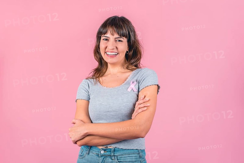 Happy woman wearing a pink breast cancer awareness ribbon while looking at camera