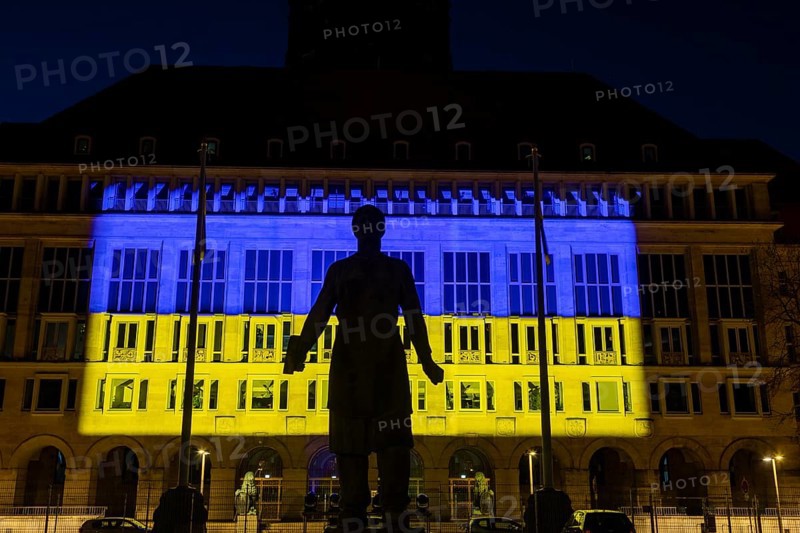 Dresden City Hall illuminated in the Ukrainian national colours, in the foreground the monument to the Trümmerfrau (rubble woman), which commemorates the rebuilding of Dresden after the Second World War