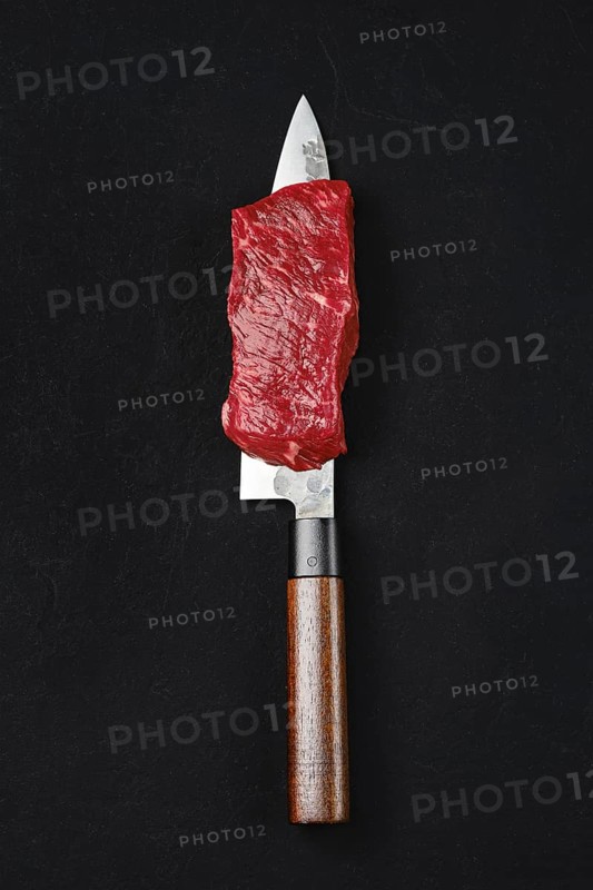 Piece of raw strip steak on the blade of knife