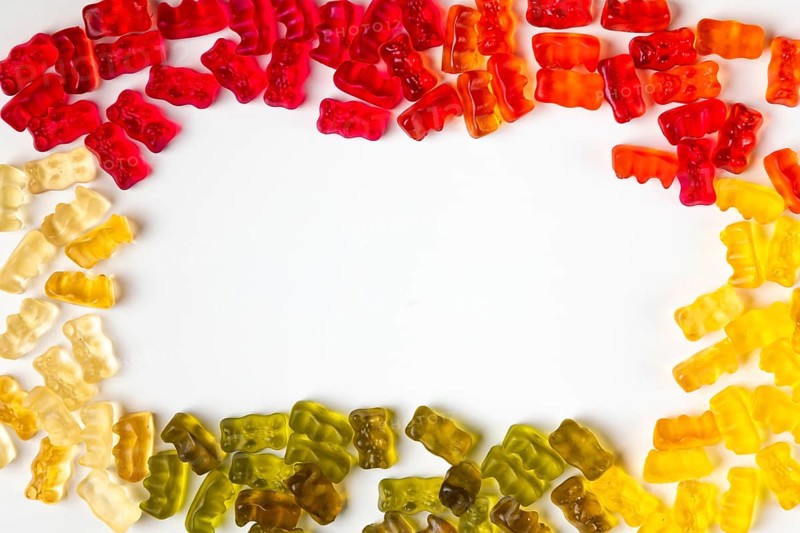 Frame made of gummy bears in assorted colours, from above, white background, copying space in the middle