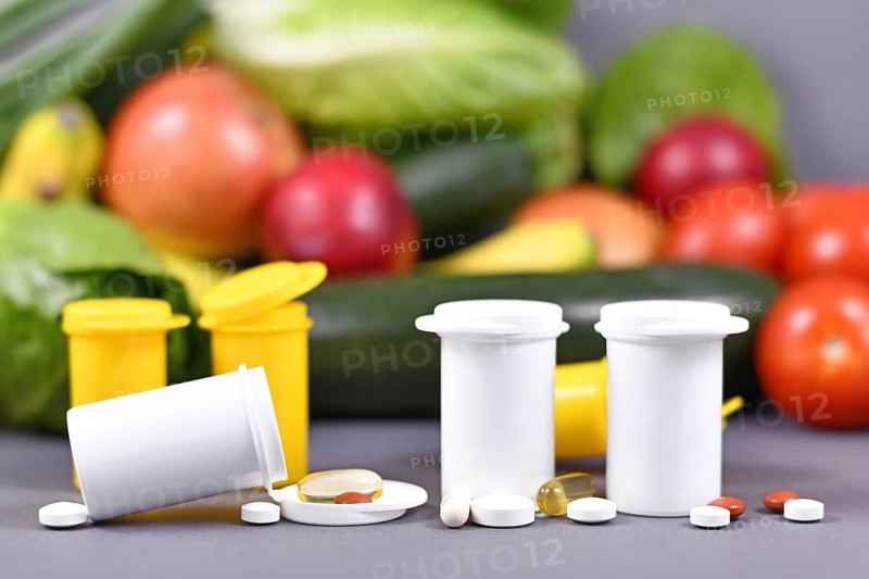 White and yellow Bottles with food nutrition supplements in front of fruits and vegetables in blurry blue background