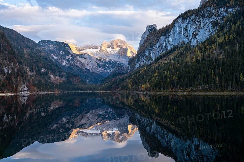 The Vordere Gosausee lake in autumn with a view of the Dachstein mountain range. The Gosaukamm on the right. Clouds in the blue sky and above the mountain peak. Reflection. Golden hour. Vorderer Gosausee, Gosau, Gosau valley, Salzkammergut, Upper Austria, Austria, Europe