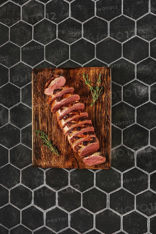 Overhead view of a seared duck breast cut on slices on wooden chopping board
