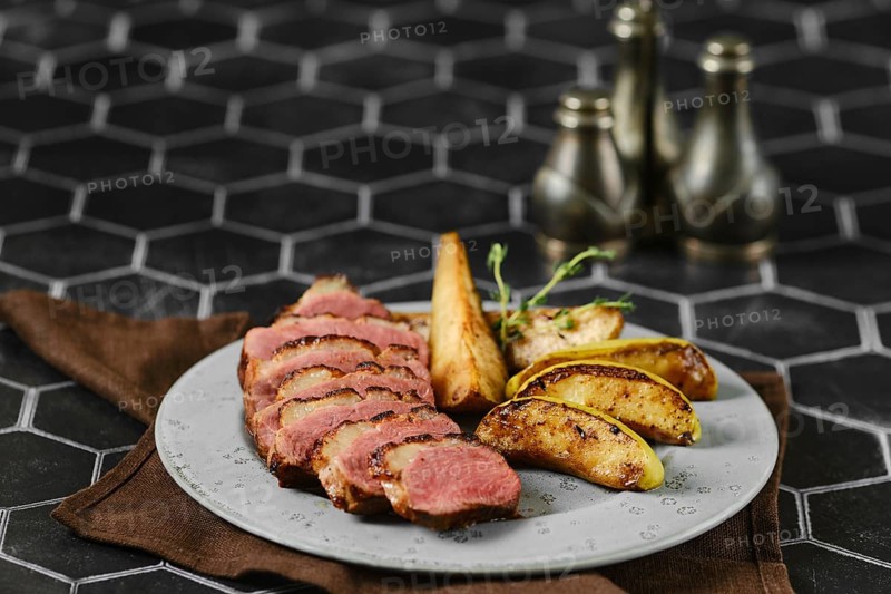 A succulent dish of duck breast, artfully sliced and arranged on a plate with roasted slices of apple and pear