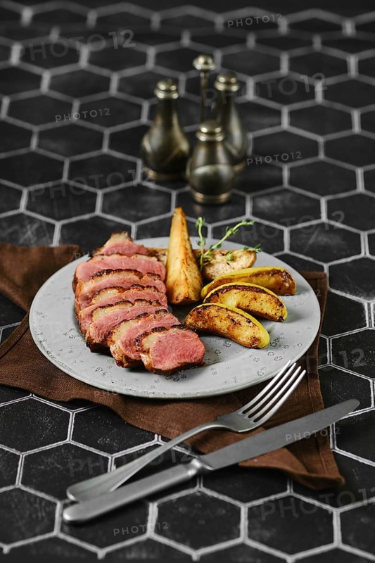 Sliced duck breast cooked to a perfect medium-rare served with caramelised apples and pears on a plate
