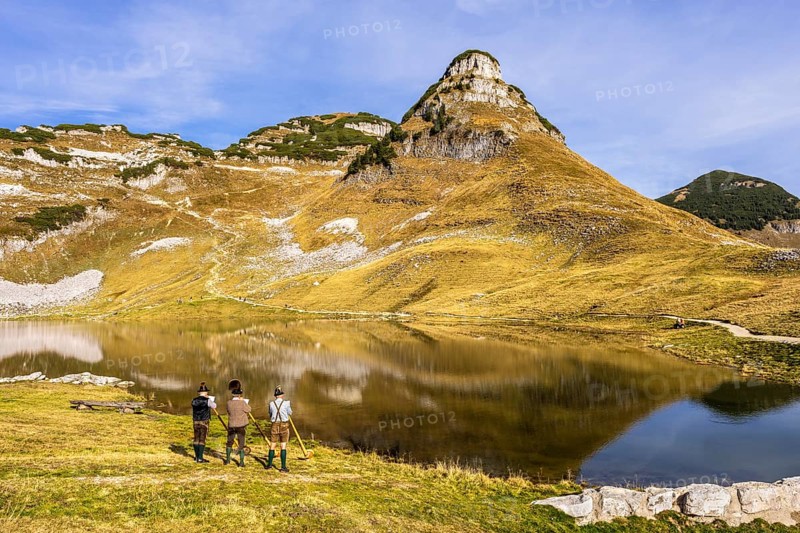 Three men play the alphorn at Lake Augstsee on Mount Loser. The Austrian alphorn trio Klangholz. Mount Atterkogel in the background. Autumn, good weather, blue sky. Reflection. Altaussee, Bad Aussee, Ausseer Land, Totes Gebirge, Styria, Upper Austria, Austria, Europe