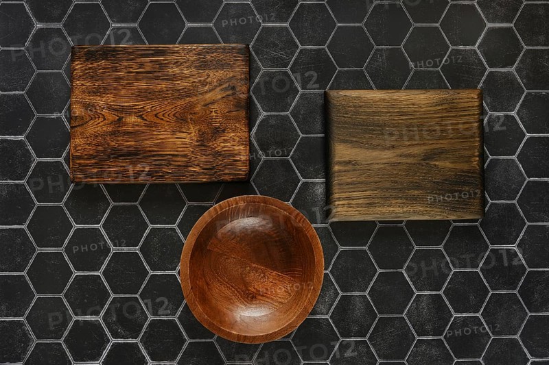 Top view of empty round wooden bowl and cutting boards on a black hexagonal tiled background