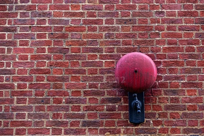 Close-up of a red brick wall with a red alarm bell