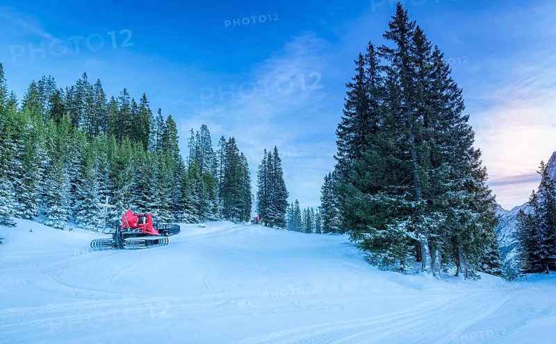 Winter scenery with lots of snow over the forestry roads in the Austrian Alps mountains and two snow groomer vehicles clearing the way