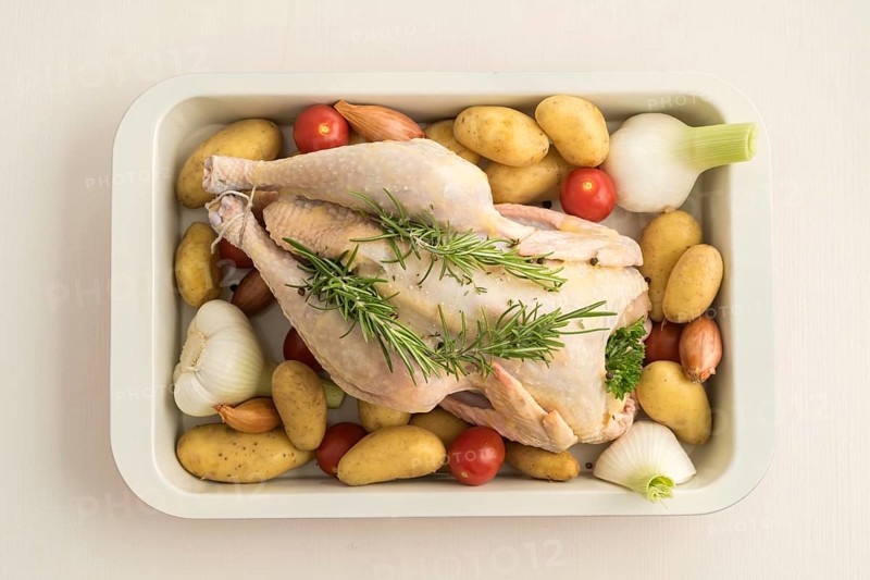 Roast chicken prepared for roasting with young garlic, shallots, parsley, cherry tomatoes, potatoes and olive oil in a casserole dish