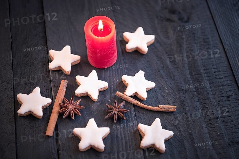 Homemade cinnamon and nuts cookies, star shaped, with decorative spices between them, on an old black wooden table, under the candlelight