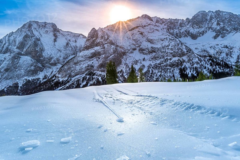 Alpine scenery on a bright day of winter, with details over the crust of ice, that lies on the surface of the Austrian Alps pastures and is due to the warmth of the sun, that shines from behind the rocky peaks