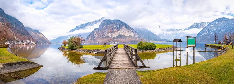 Late autumn panorama with the Hallstatter lake, the Northern Limestone Alps, the island on the lake and a wooden bridge to accesses it, in Hallstatt town, Austria, Europe