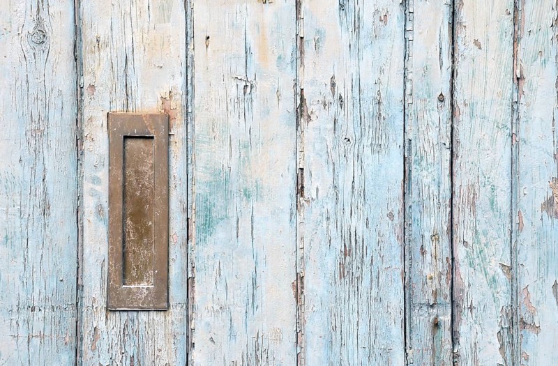 Close up of an old wooden door with blue faded paint and a rusty closed old metal brass letterbox